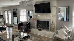 A modern living room with a fireplace, a flat-screen TV mounted above it, and a comfortable seating area with a sofa and a chair.