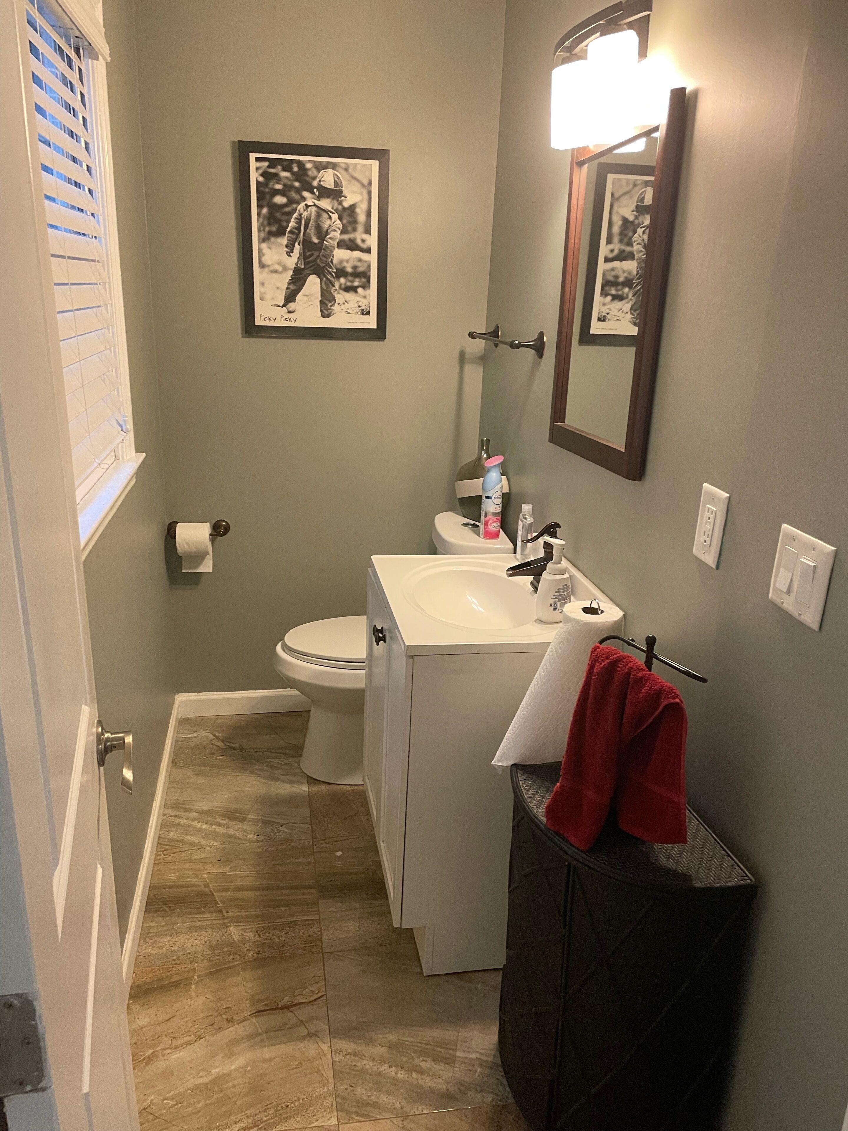 A bathroom with a toilet, sink, and mirror. There is a framed picture on the wall and a towel rack with a red towel.