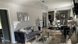 A modern living room with a grey sofa, white armchairs, and a coffee table.