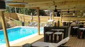 A covered outdoor area with a pool, wicker furniture, and a wooden deck.
