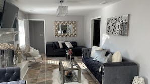 A modern living room with a black sofa, a glass coffee table, and a white furry rug.