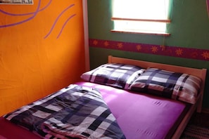 Ein Einzelbett mit kariertem Bettbezug und Kissen, ein Fenster mit Rollläden und eine Wand mit schlichtem Muster.