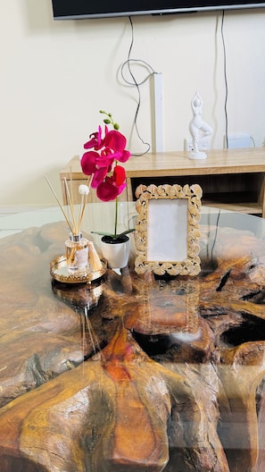 Une table en bois ornée d’un cadre décoratif, une orchidée en pot, un petit flacon et une statuette blanche.