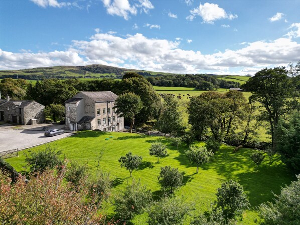 A stone building with a driveway and a grassy field in the foreground. - Riverside Mill - Luxury Cottages (Kendal)