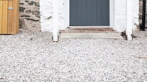 A stone building with a white exterior, a dark grey door, and a small window with a white frame. - Upper Riverside Mill - Luxury Cottages (Kendal)
