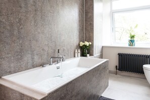 Une salle de bain moderne avec une grande baignoire, une fenêtre donnant sur un beau paysage et un radiateur.
