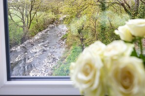 A river with rocks and trees, viewed through a window with white roses in the foreground. - Upper Riverside Mill - Luxury Cottages (Kendal)