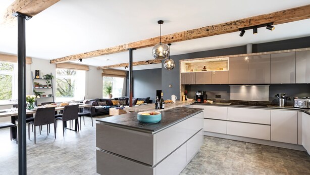 A modern kitchen with a central island, built-in appliances, and a dining area with a sofa and chairs. - Upper Riverside Mill - Luxury Cottages (Kendal)