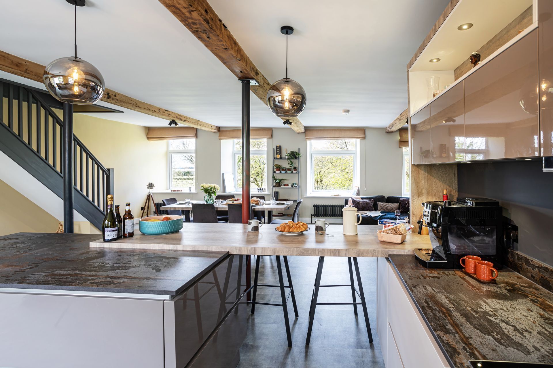 A modern kitchen with a central island, bar stools, a coffee machine, and a large window.