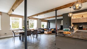 A modern kitchen with a central island, dining area with chairs, and a living room with a sofa. - Upper Riverside Mill - Luxury Cottages (Kendal)