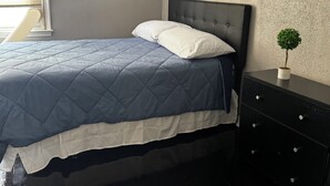 Quarto com cama, cómoda, planta em vaso e janela com persianas.