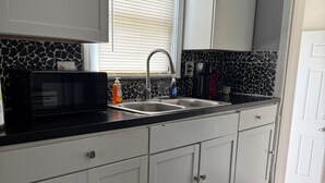 Uma cozinha com armários brancos, bancada preta, tapete vermelho e uma janela com persianas.