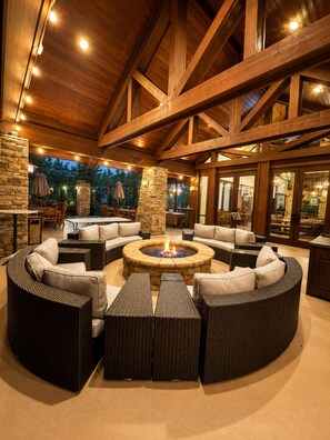 A covered outdoor seating area with stone pillars, wicker furniture, and a central fire pit. - Torreon Golf Cabin • 2 King Suites • Sleeps 8 • Dog Friendly (Show Low)