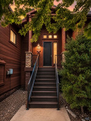 A wooden house with a staircase leading to a dark door, surrounded by trees and a stone wall. - Escape the Arizona Heat + 2 King Suites + Bunk Room (Show Low)