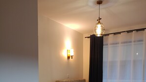 Ett sovrum med en säng, en soffa, ett litet bord, en vägglampa och ett fönster med gardiner.