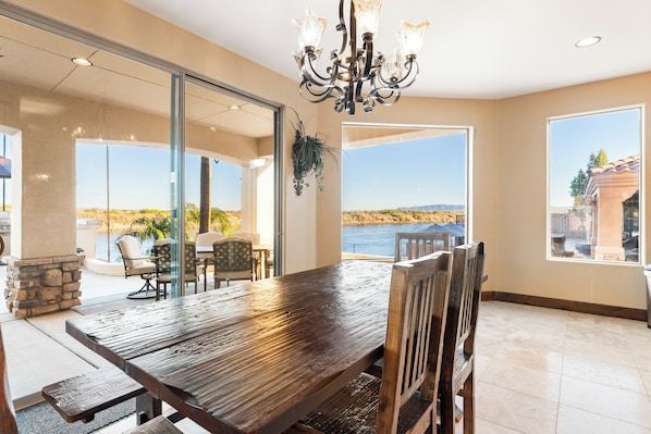 A dining area with a large wooden table, chairs, a chandelier, and a view of the outdoors.