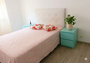 Quarto com cama, duas mesas de cabeceira, uma planta em vaso e uma cômoda azul-turquesa.