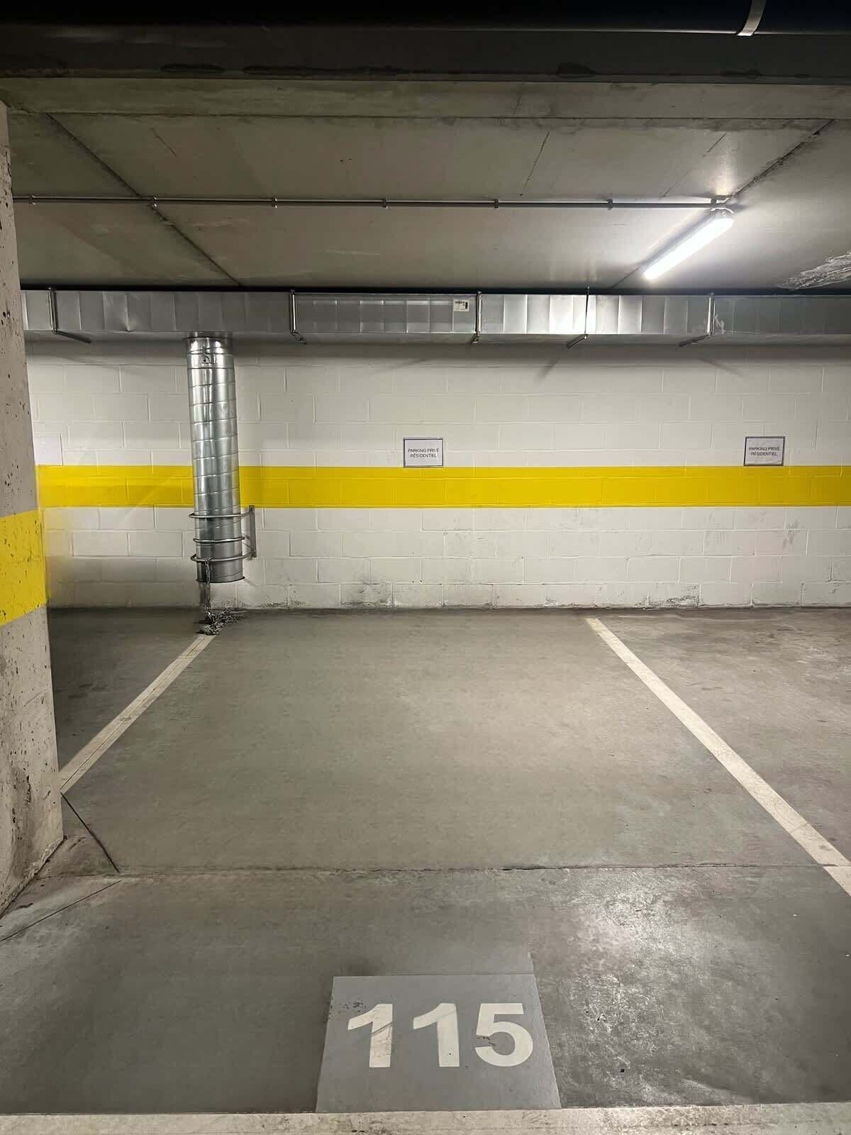 Een parkeergarage met een betonnen vloer, aangegeven parkeerplaatsen en een ventilatiekanalen.