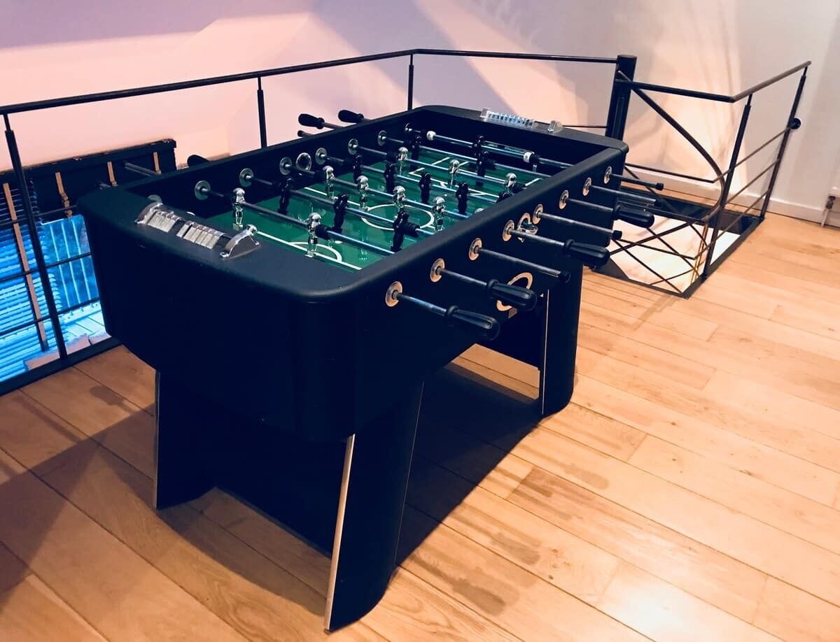 A foosball table with a metal frame and a control panel, placed on a wooden floor.
