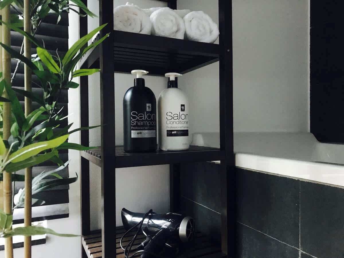 Een badkamerplank met toiletartikelen, een haardroger en een bamboeplant.