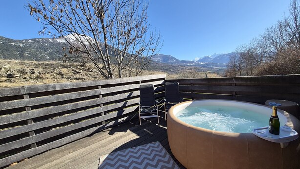 A wooden deck with a hot tub, chairs, and a bottle of champagne.
