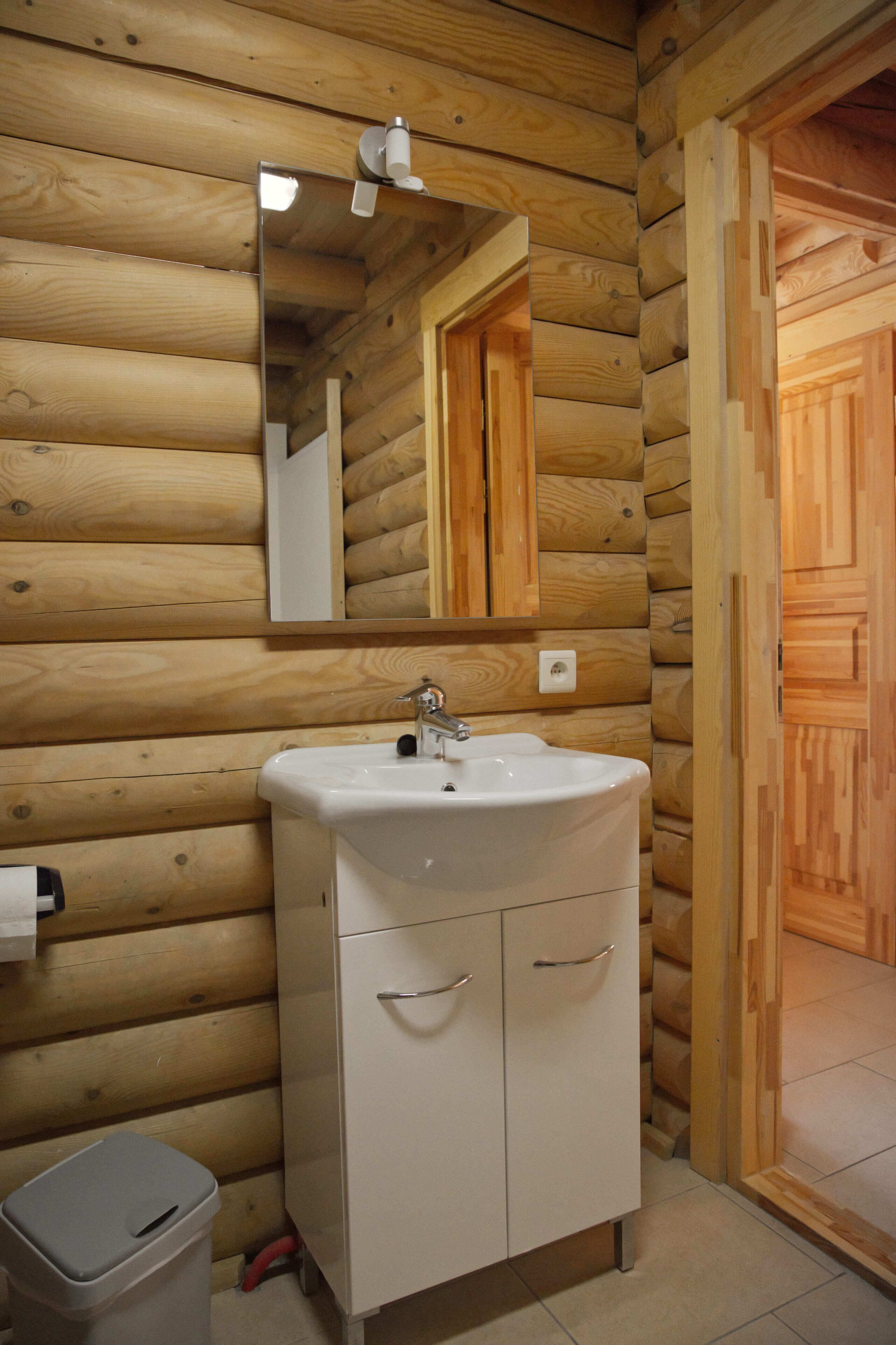 A wooden cabin-style bathroom with a sink, mirror, and cabinets.