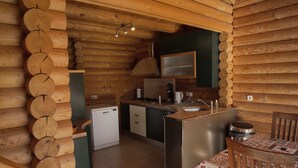 A log cabin interior with a kitchen area, a dining table with chairs, and a small refrigerator.
