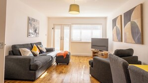 A modern living room with a grey sofa set, a small ottoman, a TV, and abstract wall art. - Paisley with Parking & Balcony - Pass the Keys (Paisley)