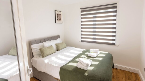 A bedroom with a bed, a window with blinds, a framed picture on the wall, and a towel on the bed. - Paisley with Parking & Balcony - Pass the Keys (Paisley)