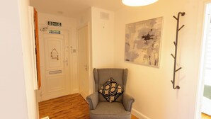 A hallway with a grey armchair, a wall-mounted artwork, and a door with exit signs. - Paisley with Parking & Balcony - Pass the Keys (Paisley)