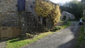 A stone building with a wooden door, a metal balcony, and a gravel path. - Country Hideaways | Turnsyke Barn | Newbiggin (Leyburn)