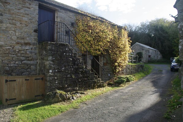 A stone building with a wooden door, a metal balcony, and a gravel path.
