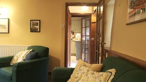 A living room with two green sofas, a radiator, and a door leading to a kitchen. - Country Hideaways | Turnsyke Barn | Newbiggin (Leyburn)