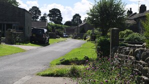 A rural road with stone walls, a stone building, and a parked car. - Country Hideaways | Turnsyke Barn | Newbiggin (Leyburn)