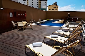 A rooftop pool area with lounge chairs and a small table, surrounded by buildings. - Loft em Ponta Negra com vista para o mar (Natal)