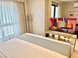 Een hotelkamer met een bed, een televisie op een houten standaard, een raam met gordijnen en een kapstok.
