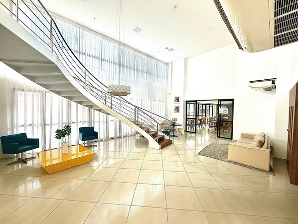 A spacious lobby with a central staircase, a reception desk, and a seating area.