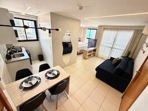 A modern living room with a dark blue sofa, a dining area with a table set for two, and a kitchen area with a sink and stove.
