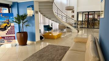 A modern hotel lobby with a staircase, a seating area, and a large potted plant.