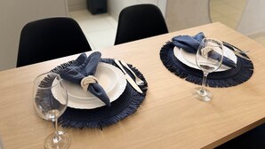 Une table à manger dressée avec des assiettes, des couverts et des verres à vin, avec un haut-parleur et un mur carrelé en arrière-plan.