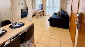 Une chambre d’hôtel moderne dotée d’un coin repas, d’un canapé, d’une télévision et d’une grande fenêtre avec des rideaux.