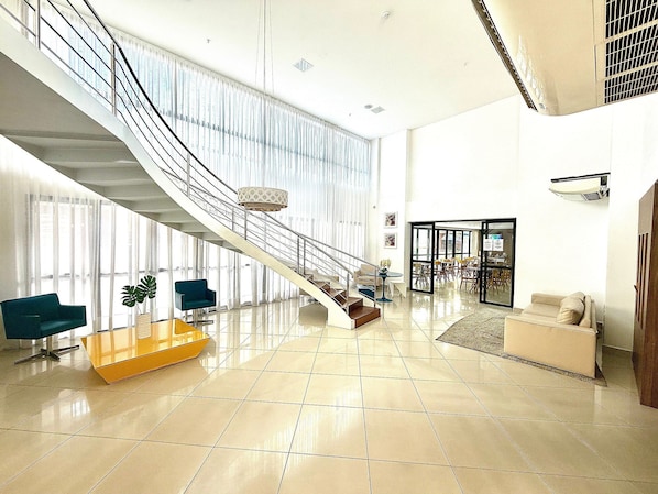 A spacious lobby with a staircase, a reception desk, and seating areas.