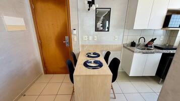 A compact kitchen with a dining area, featuring a wooden door, a small island with a sink, and basic amenities.