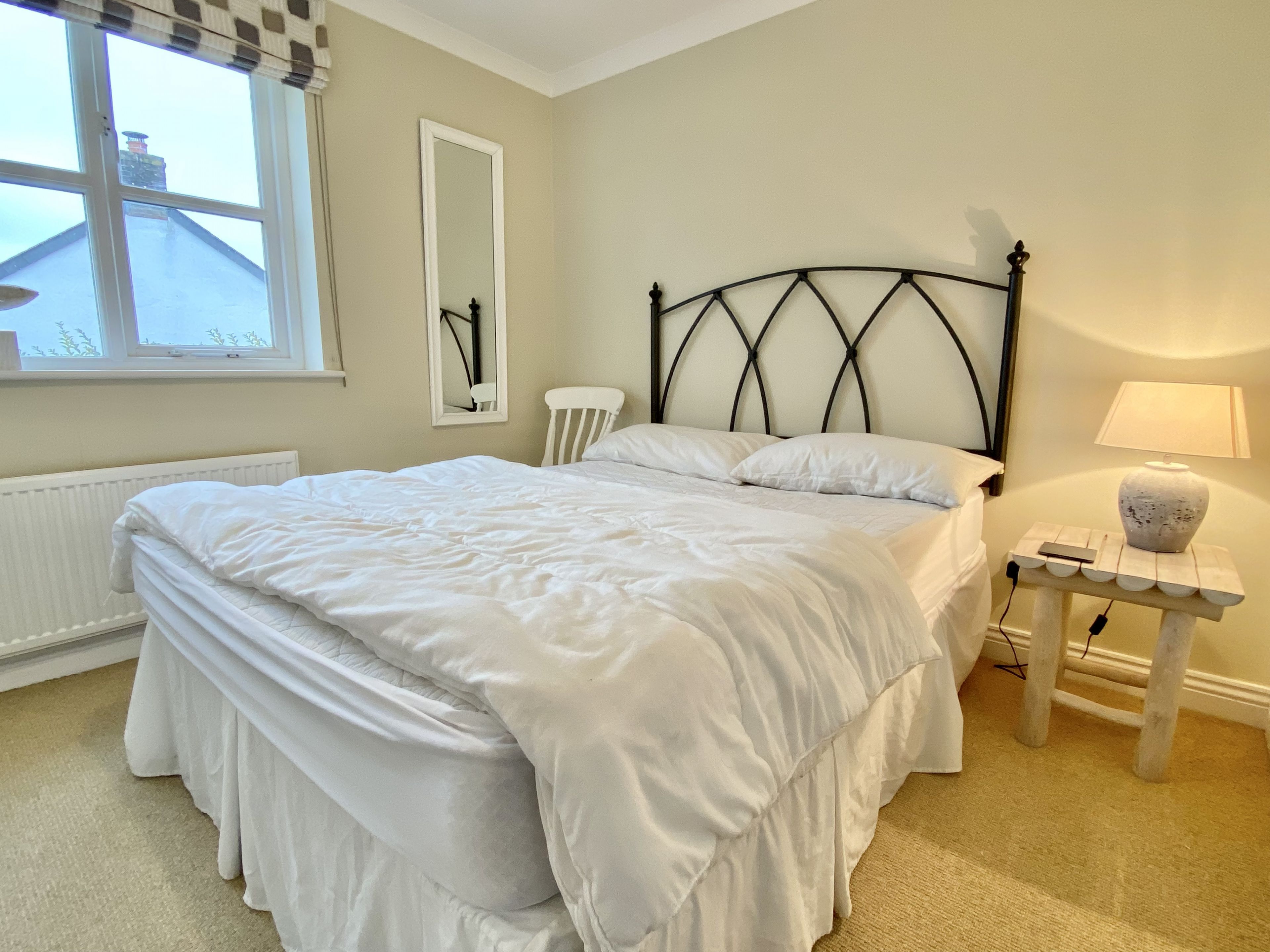 Een slaapkamer met een bed, nachtkastje met lamp, een stoel, een raam en een radiator.
