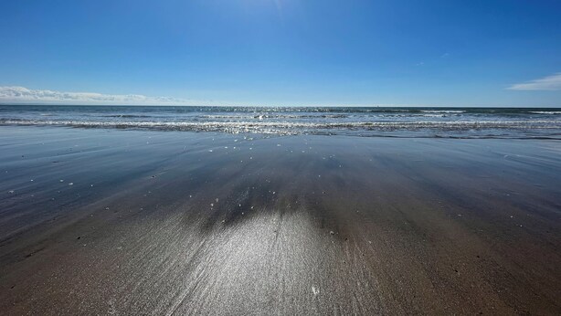 Una playa con cielo despejado y luz solar que se refleja en la arena.