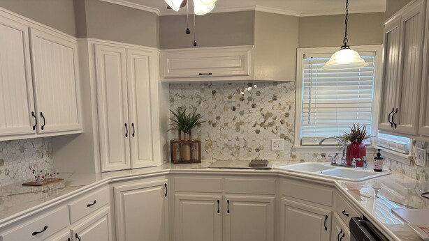 A kitchen with white cabinetry, a hexagonal tile backsplash, a dishwasher, and a window with blinds.