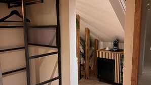 Un intérieur moderne avec une étagère en bois, un coin cuisine doté d’un réfrigérateur noir et un luminaire suspendu.