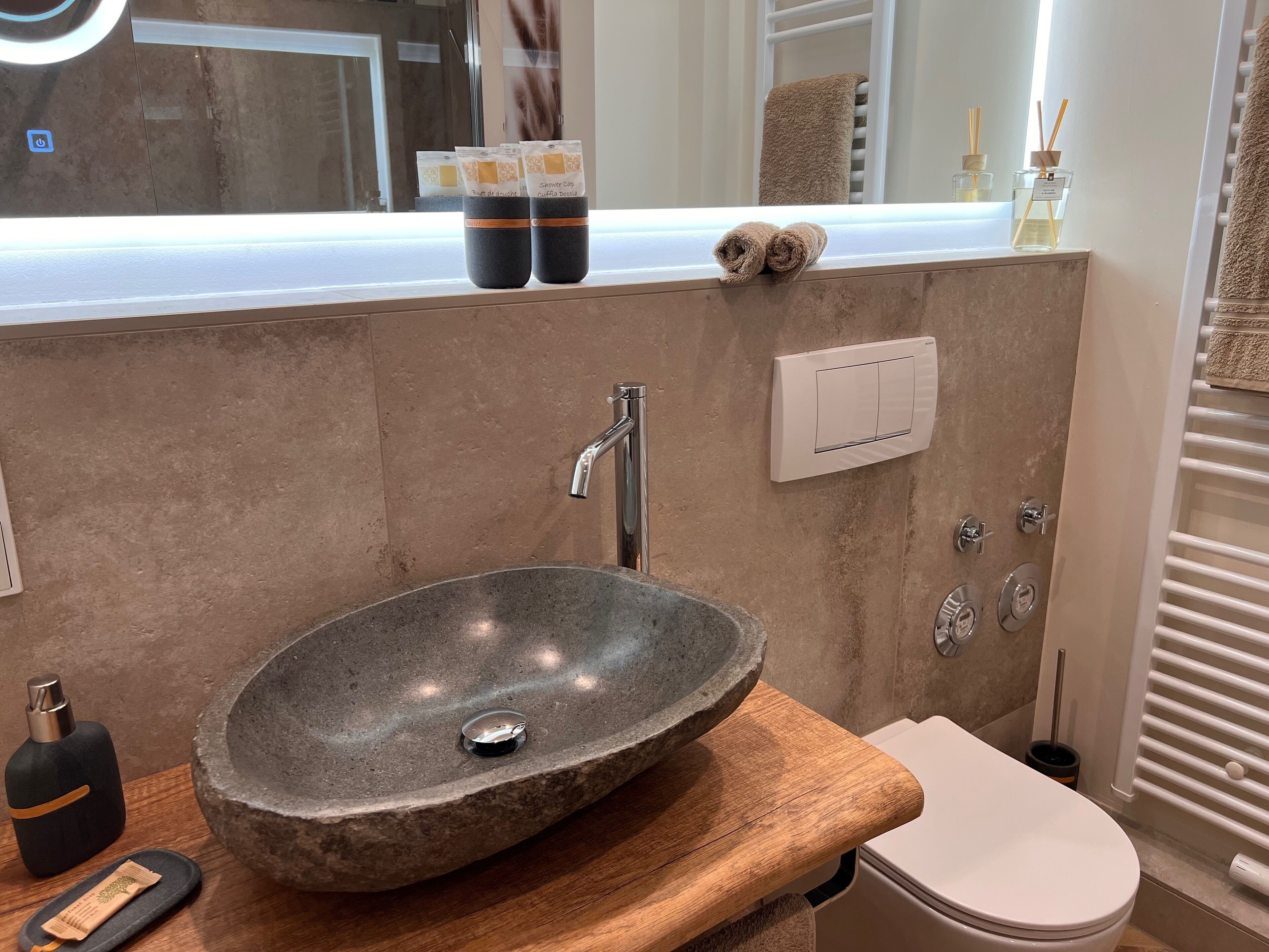 Een badkamer met een stenen wasbak, een houten aanrechtblad, een toilet, een spiegel en een handdoekhouder.