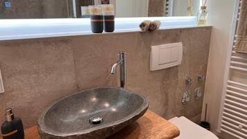 Een badkamer met een stenen wasbak, een houten aanrechtblad, een toilet, een spiegel en een handdoekhouder.