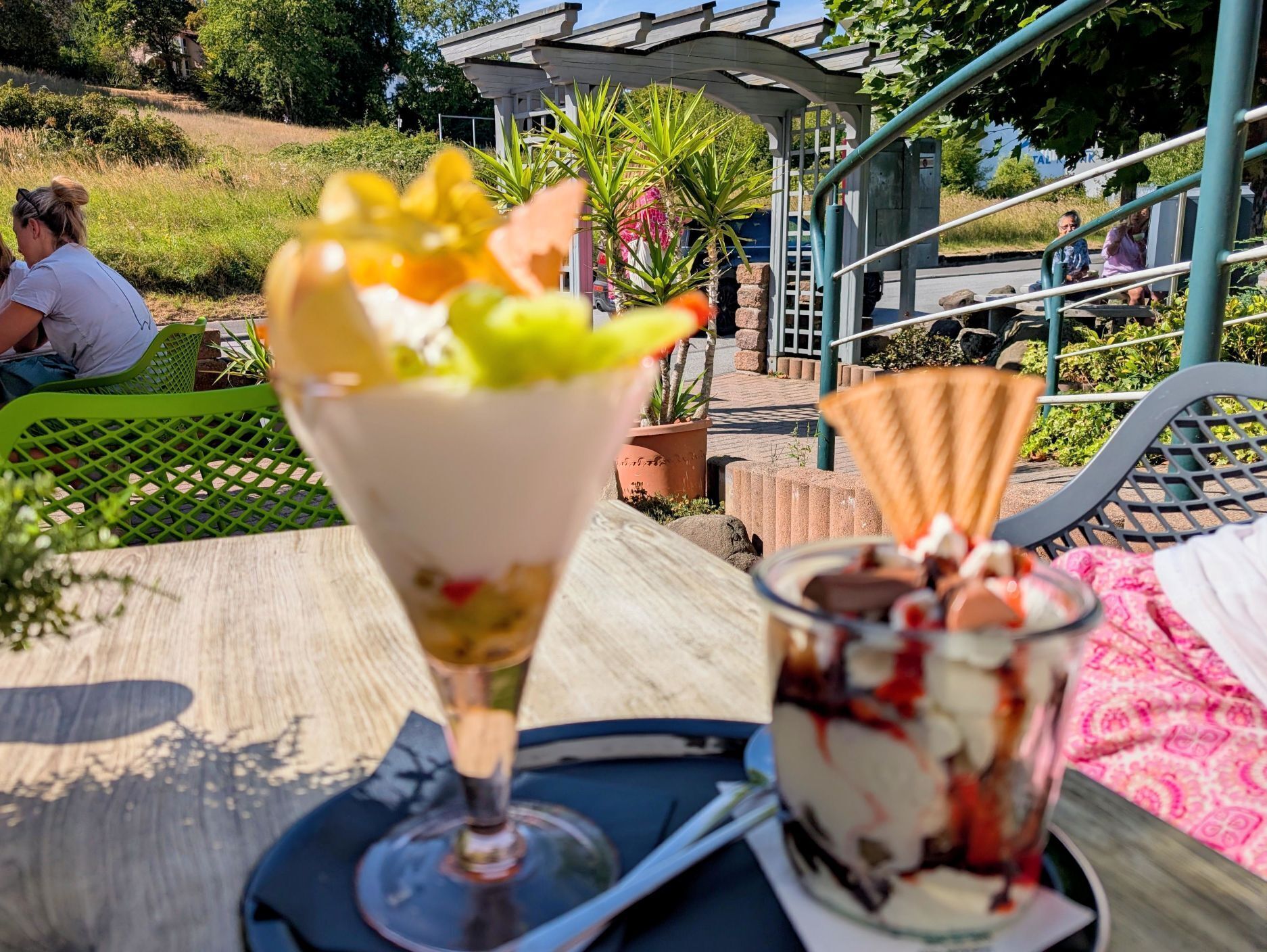 Dessert auf einer Serviertablett mit einem Glas Wein, Außenbereich und Blick auf einen Garten.